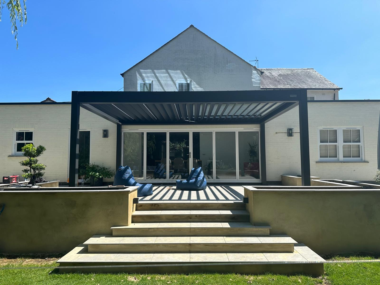 Rear of a white rendered house with bi-fold doors, aluminium pergola and raised sandstone patio steps built by DBD Builders Ltd